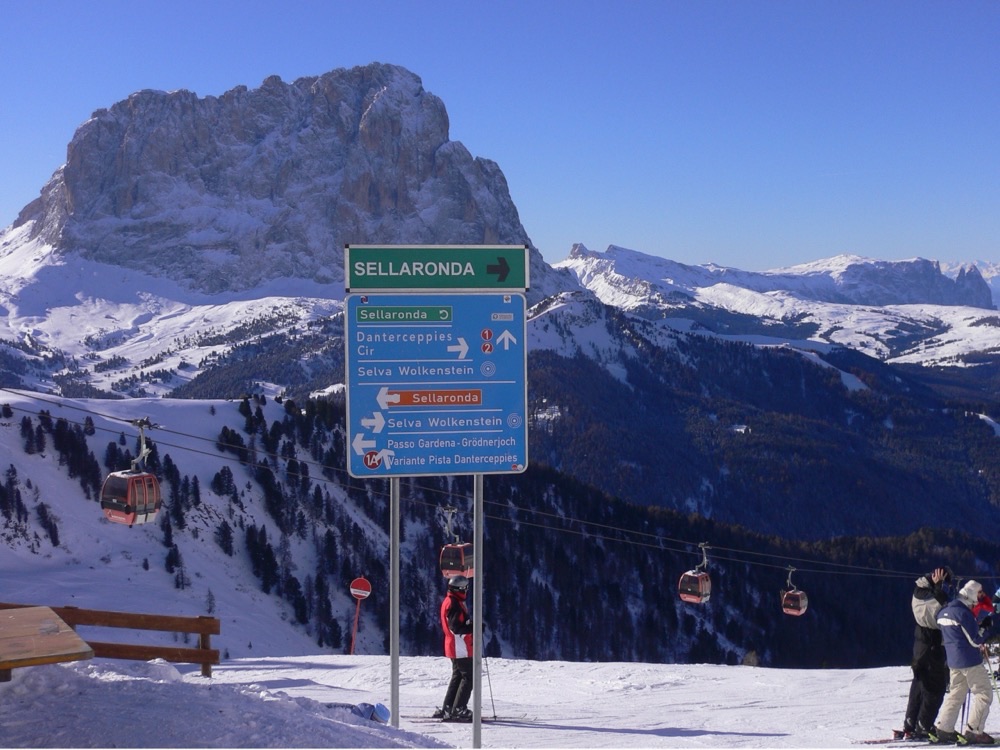 A Sella Ronda signpost above Selva with gondolas and the Sassolungo behind