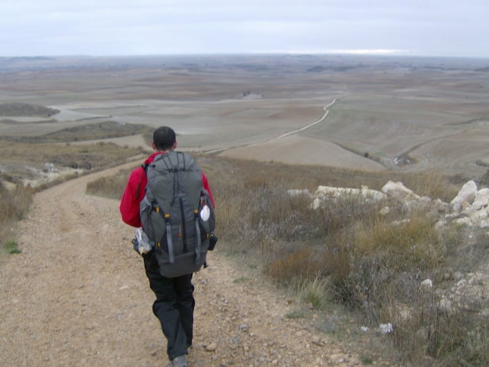 A pilgrim with a backpack walking a track across wide open country