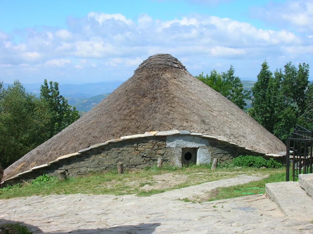 A round stone palloza with a thatched roof in O Cebreiro