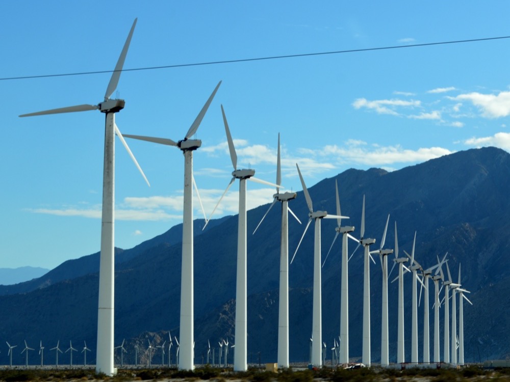 Rows of white wind turbines in the San Gorgonio Pass with the mountains behind