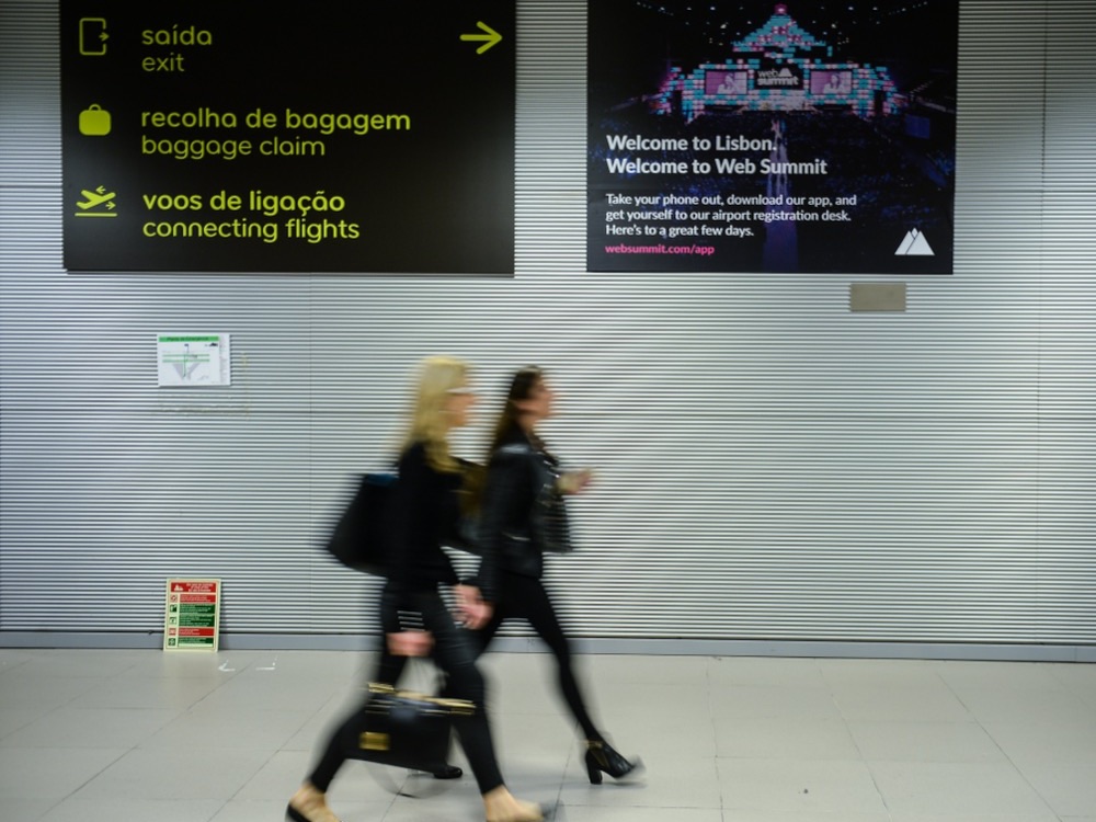 A Web Summit welcome sign beside the baggage-claim signs at Lisbon Airport