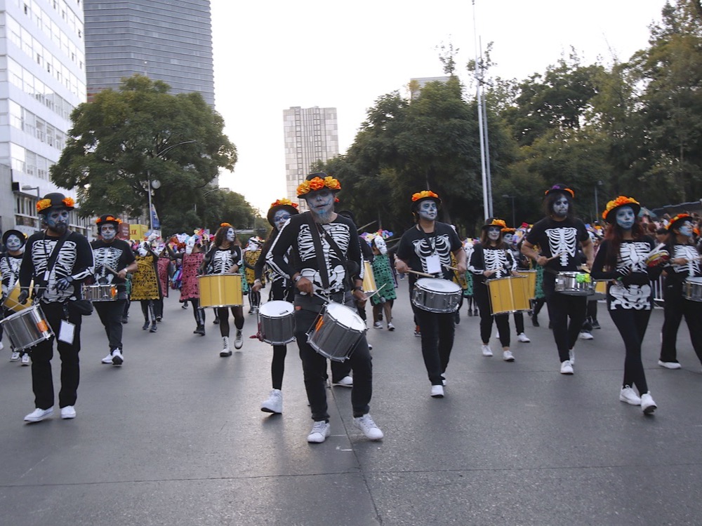 A drum corps in skeleton costumes marching between El Caballito and Avenida Juárez