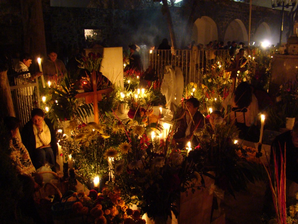 Graves covered in candles and marigolds at night in the cemetery of Mixquic