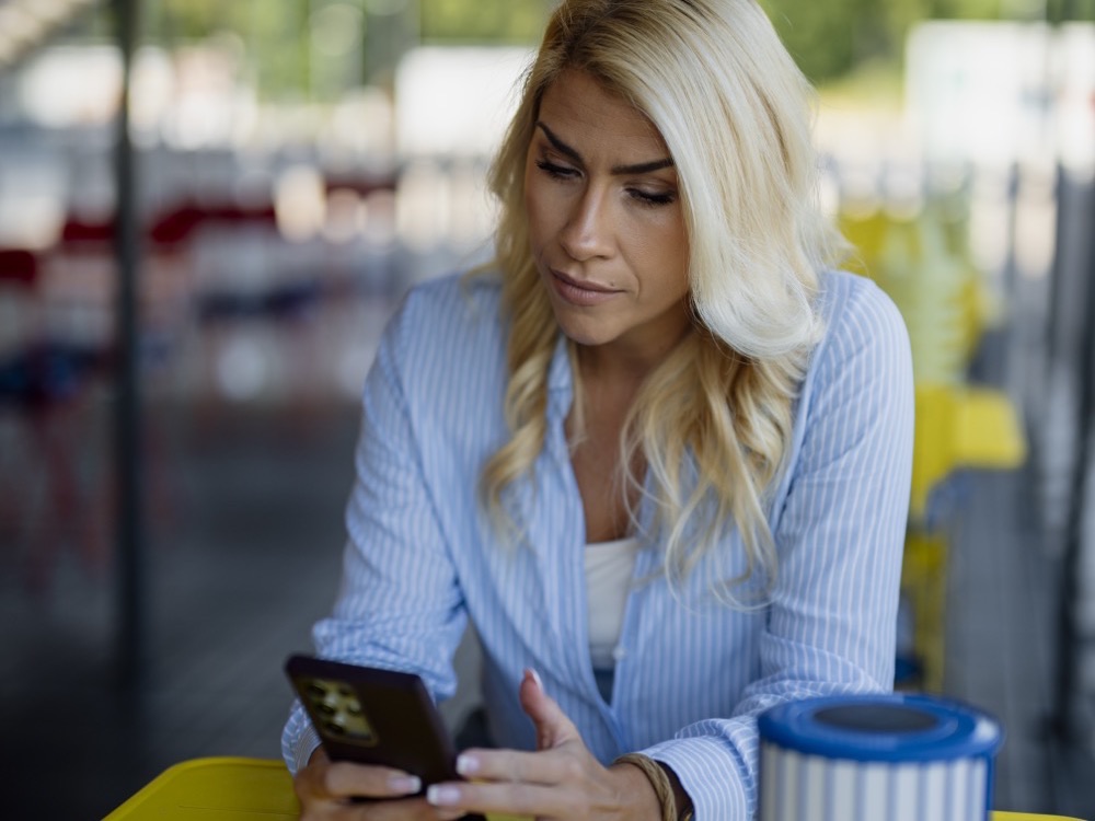A woman at a yellow table in an outdoor café looking at her smartphone
