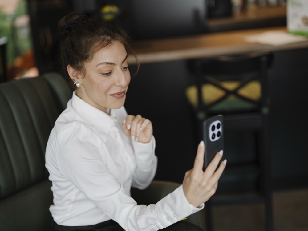 A woman sitting in a café holding up her smartphone for a video call