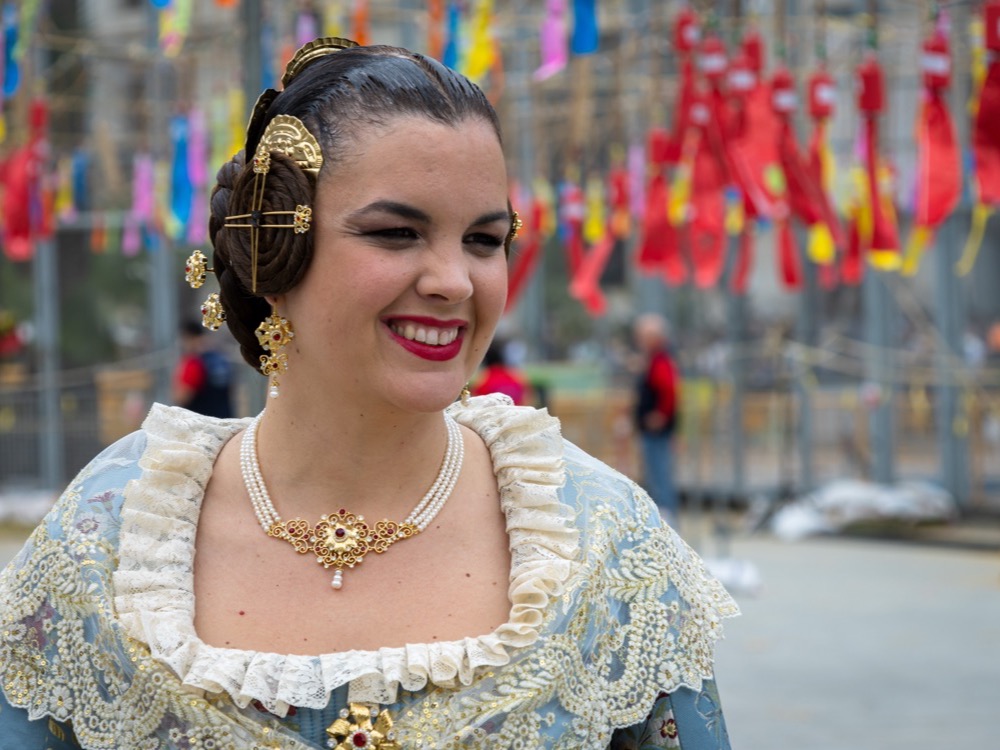 A fallera in traditional Valencian dress in the Plaza del Ayuntamiento, the red mascletà racks strung up behind her