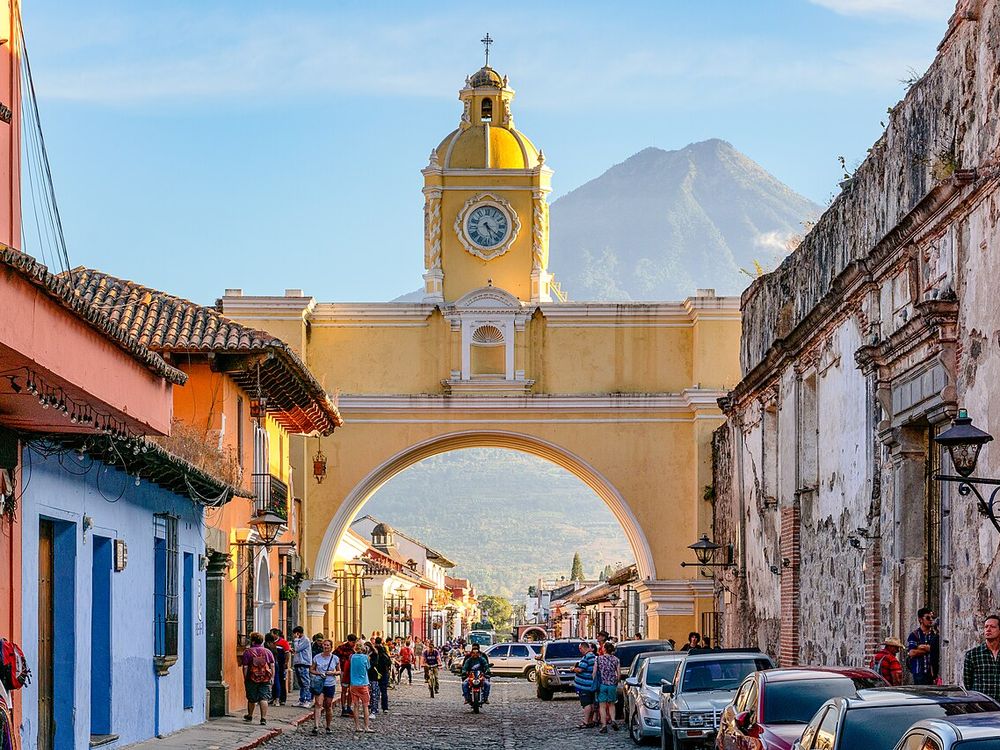 The yellow Santa Catalina arch in Antigua Guatemala with a volcano behind