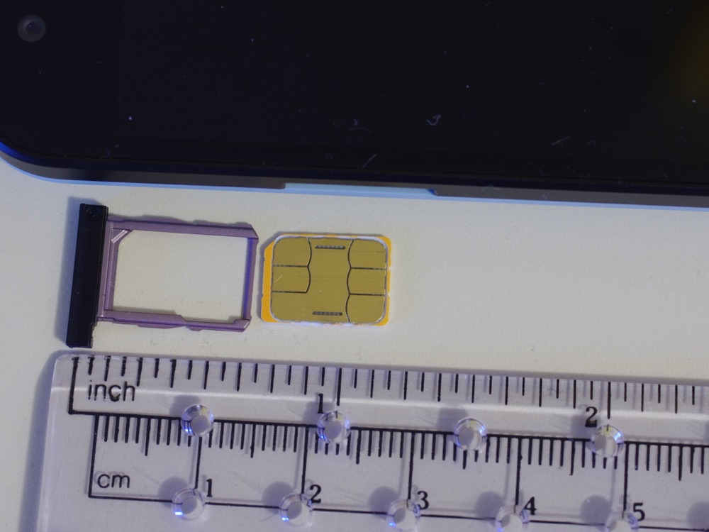 A nano SIM card next to its tray, on a ruler marked in inches and centimetres