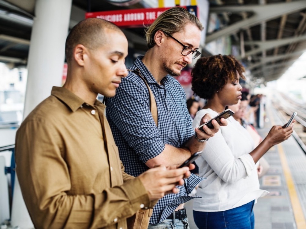 Three people at a railway station looking at their smartphones