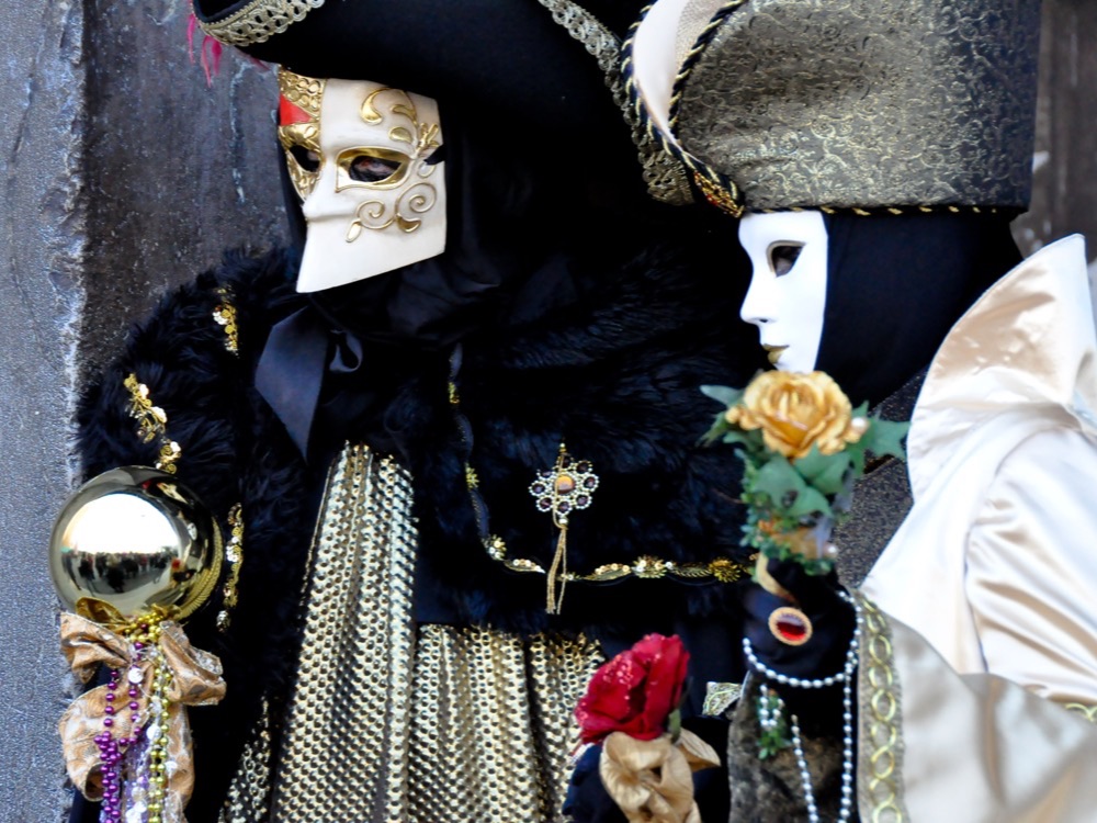 Two people in full carnival costume and white masks in Venice